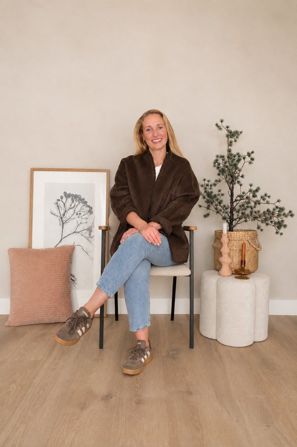 Suzanne van Suustain zit in een passende setting met een schilderij, kussen, kandelaars, poef en een plant en kijkt in de camera.
